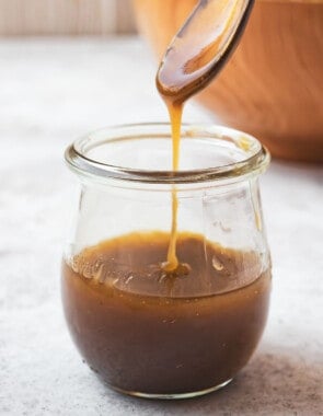 The balsamic vinaigrette being drizzled from a small serving spoon into a jar with the rest of the balsamic vinaigrette recipe.