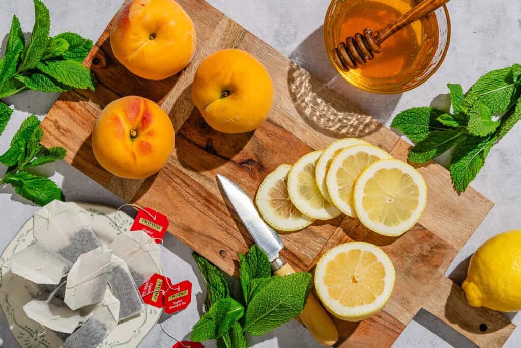 Ingredients for peach tea including peaches, lemon, mint, bags of tea and honey.