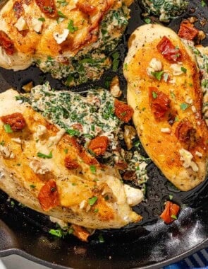 Three spinach stuffed chicken breasts in a cast iron skillet next to a cloth napkin.