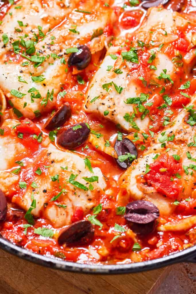 A close up of provençal fish in a cast iron skillet.