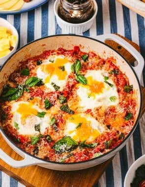 A skillet of eggs in purgatory next to a jar of jam and other various table settings.