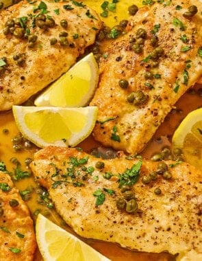 Chicken piccata with lemon wedges in a skillet with a wooden spoon.