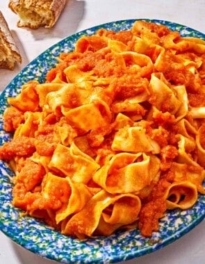Pasta tossed with lentil bolognese on a platter next to a crusty baguette torn in half.