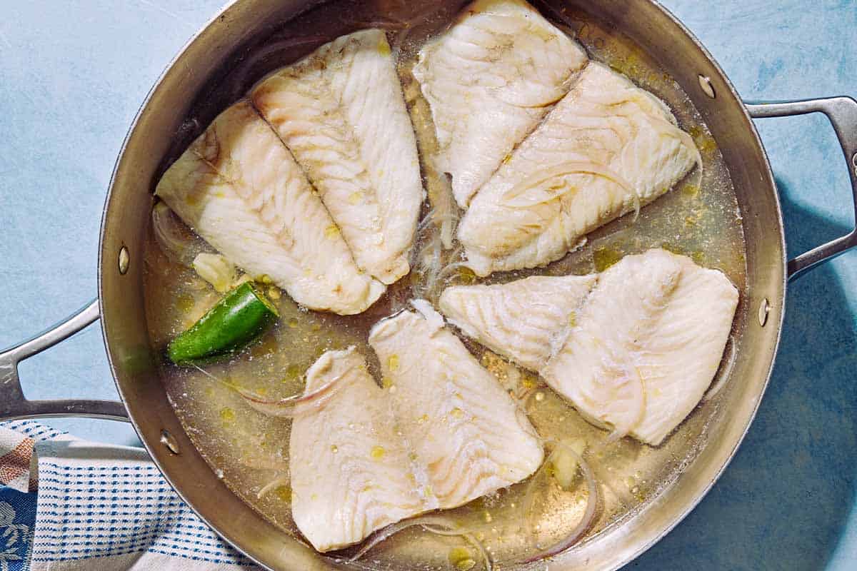 4 flounder fillets being poached in water in a tall sided skillet.