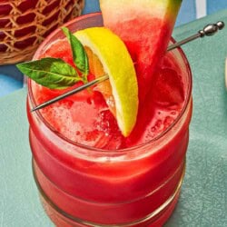 A glass of watermelon lemonade garnished with basil and slices of watermelon and lemon.