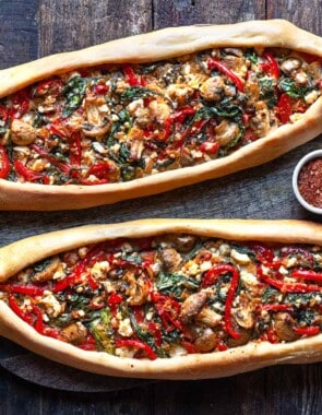Two baked turkish pide on a serving board with a bowl of aleppo pepper.